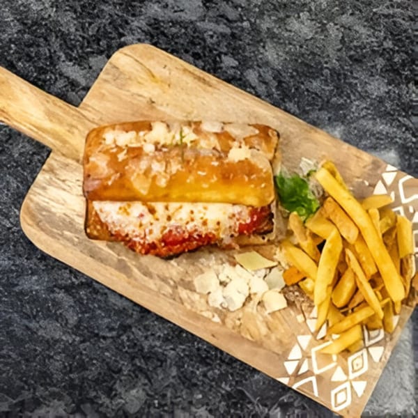 Bella Ciao's chicken parmesan sandwich with melted cheese and marinara, served with golden fries on a wooden board.