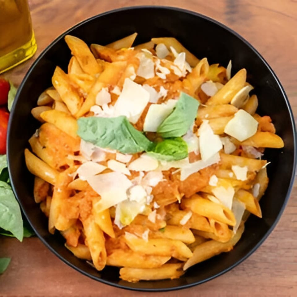 Penne pasta with tomato sauce, parmesan cheese, and basil in a black bowl.