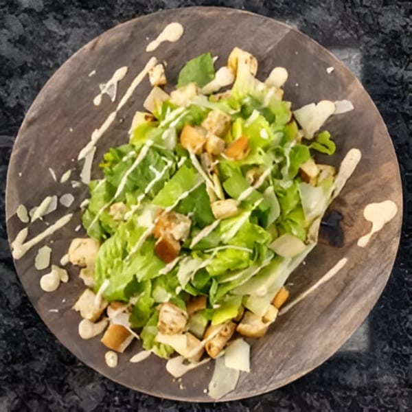 Caesar salad with crisp romaine lettuce, croutons, parmesan, and creamy dressing on a wooden plate.