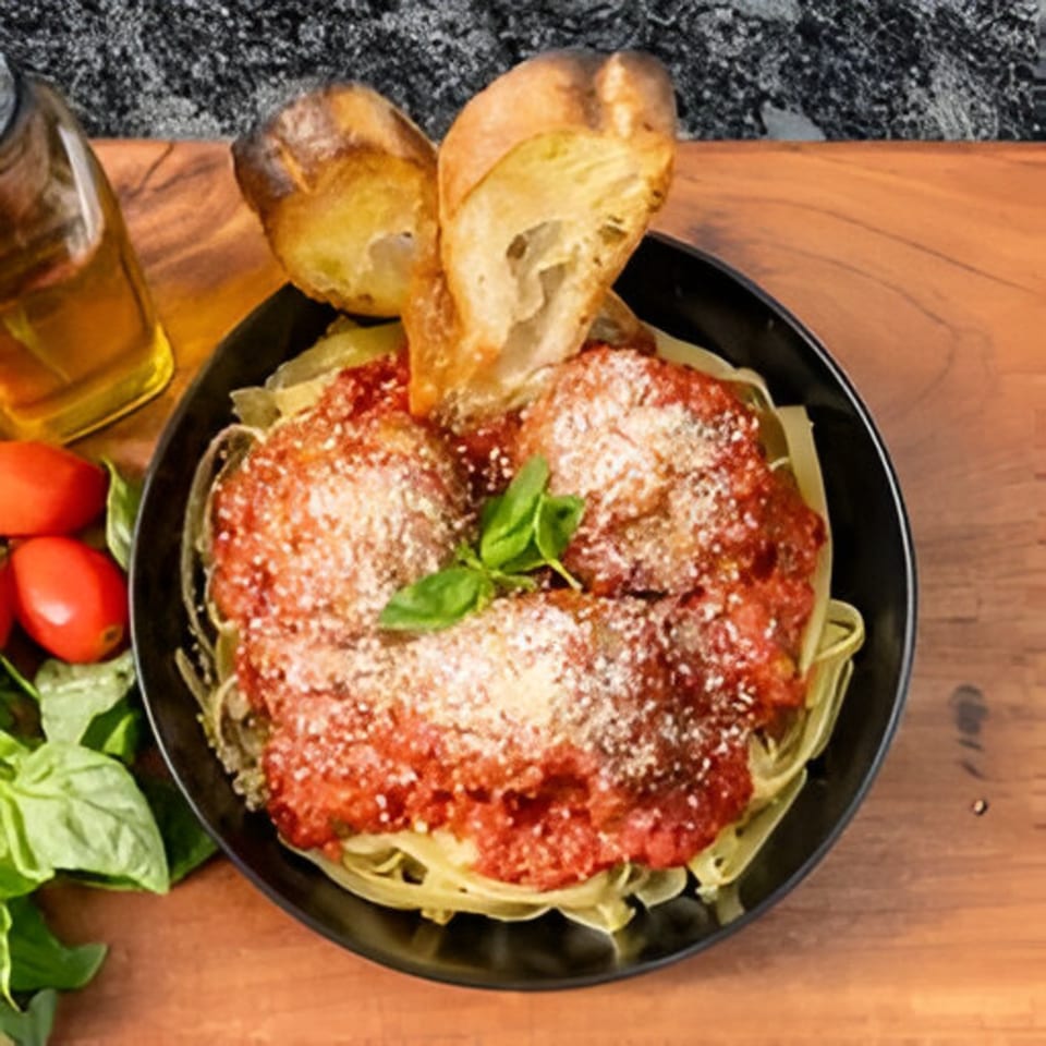 Bella Ciao's pasta with meatballs, red sauce, parmesan, basil, and bread on a wooden table.