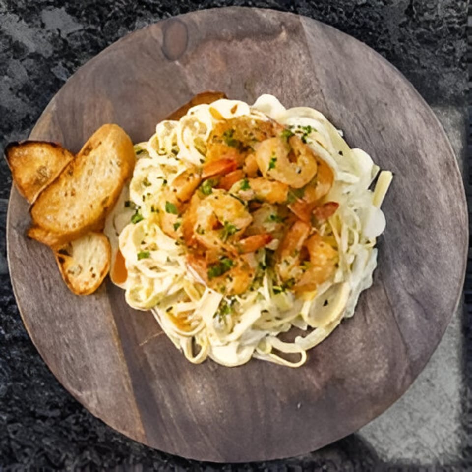 Creamy pasta with shrimp and toasted bread on a round wooden board.
