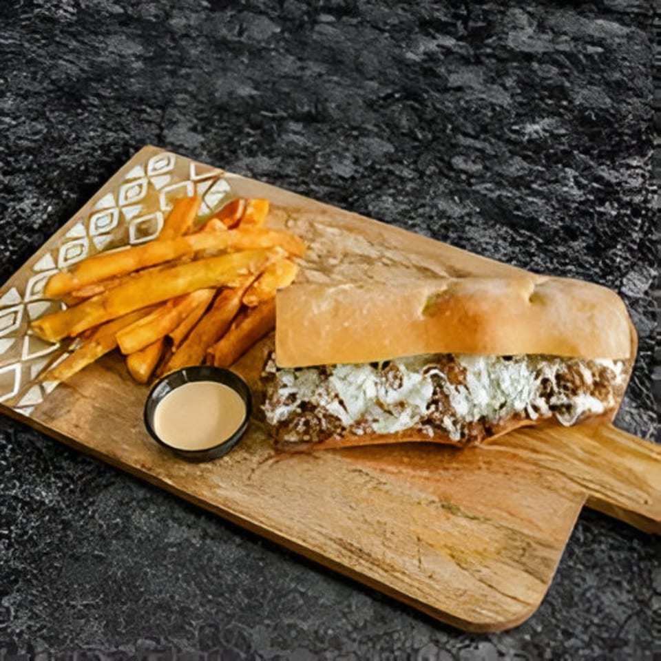 A Bella Ciao cheesesteak with fries and dipping sauce on a wooden board.